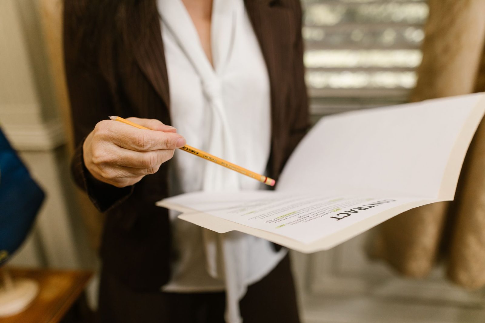 A businesswoman holds a contract and points to a clause with a pencil in a legal office setting.
