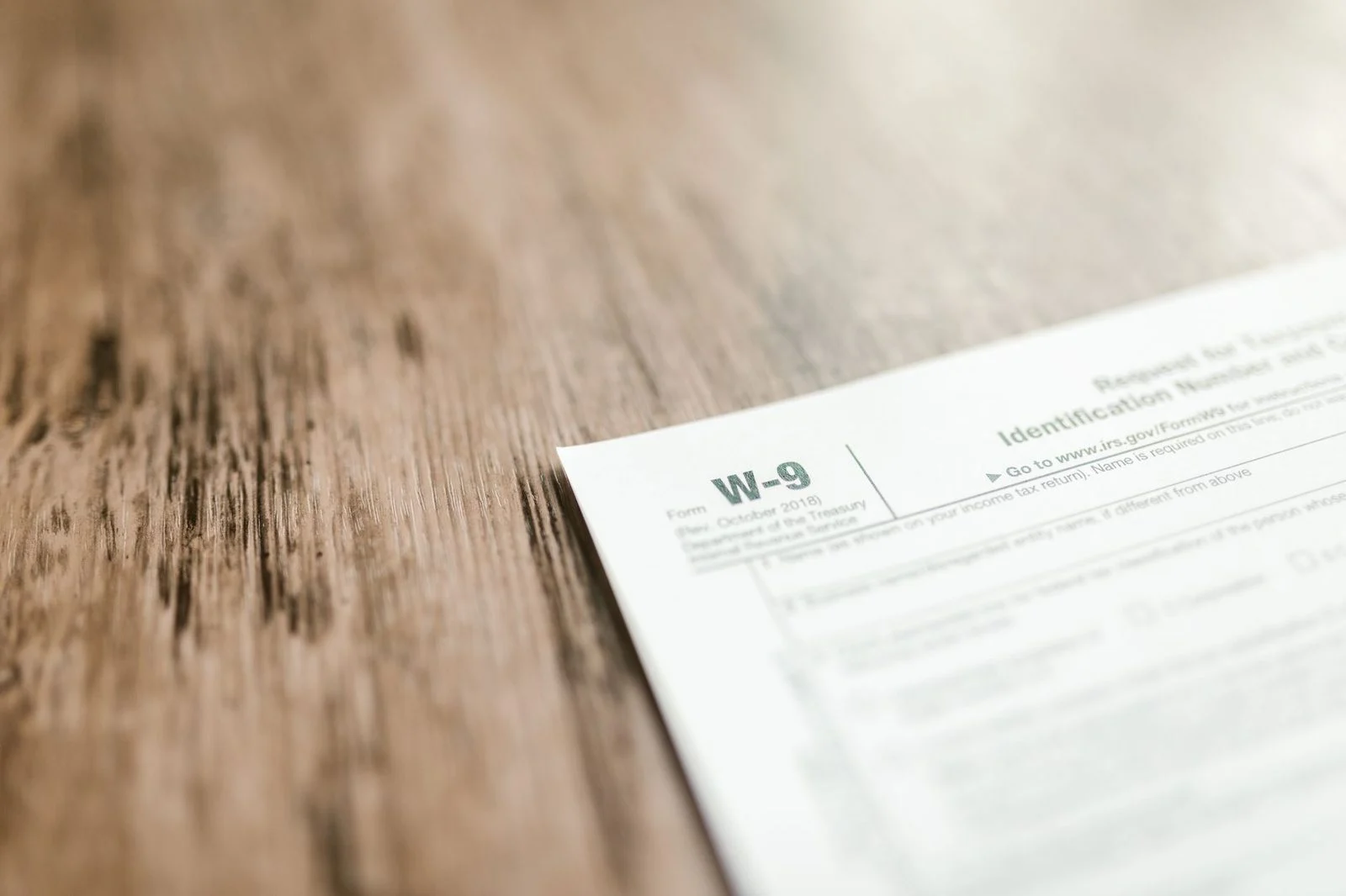 A close-up of a blank IRS W-9 tax form resting on a wooden desk.