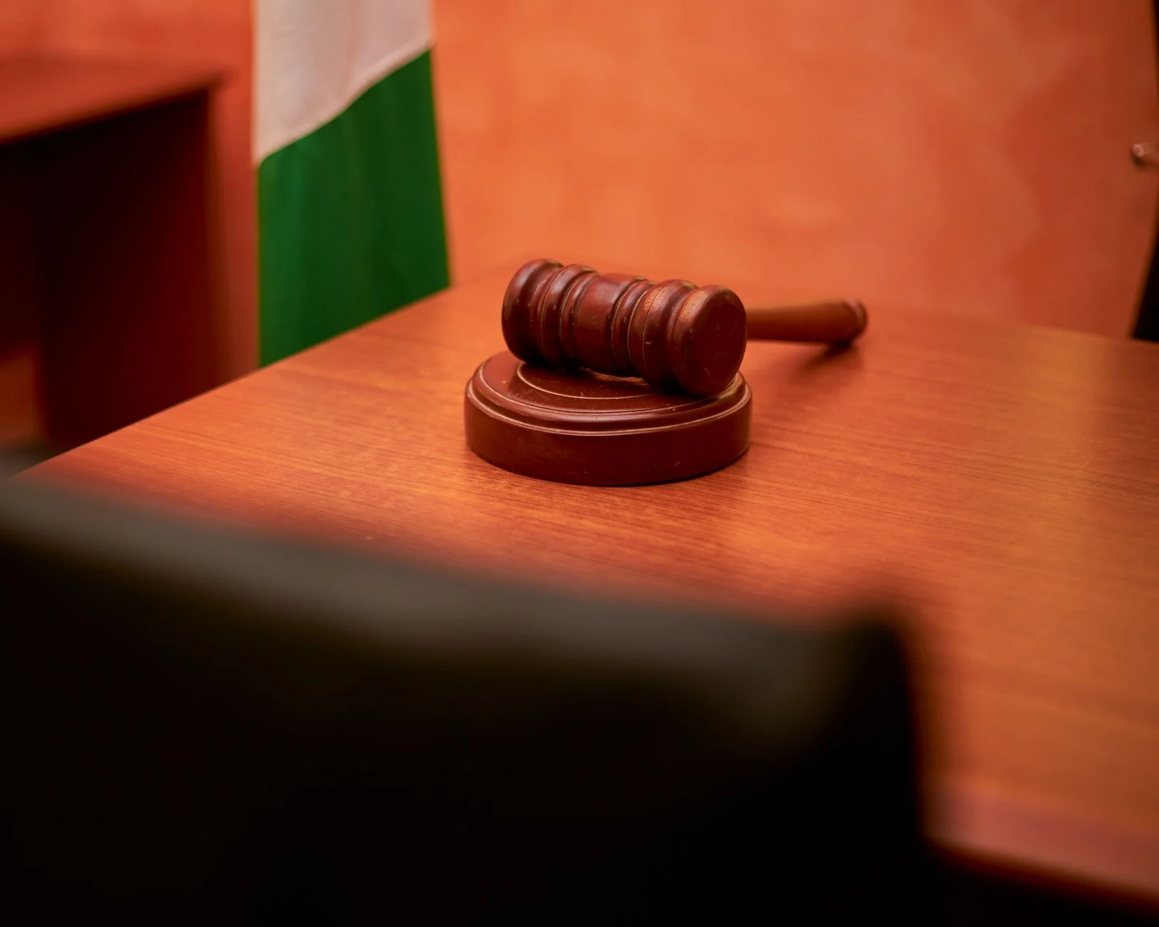 A close-up of a gavel resting on a courtroom desk.