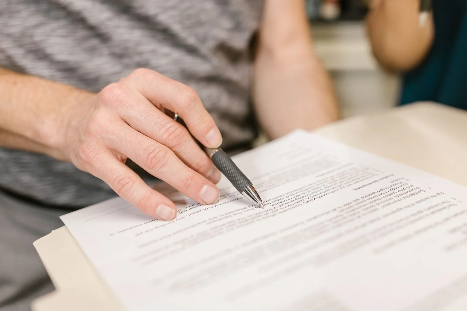 A close-up of a hand signing a legal document with a pen indoors.