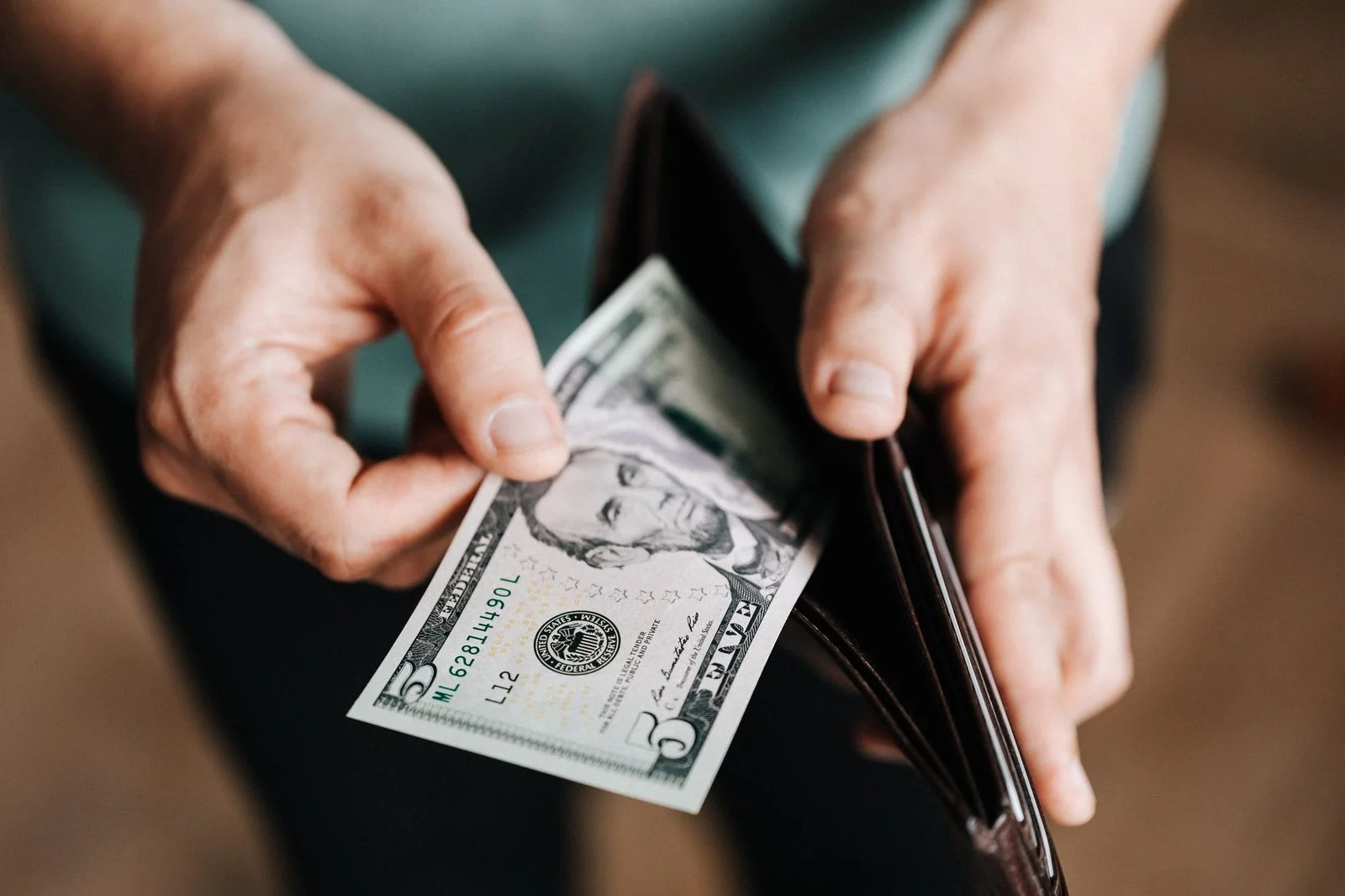 A close-up of a man in casual clothes pulling dollar bills from his wallet to pay at a shop.