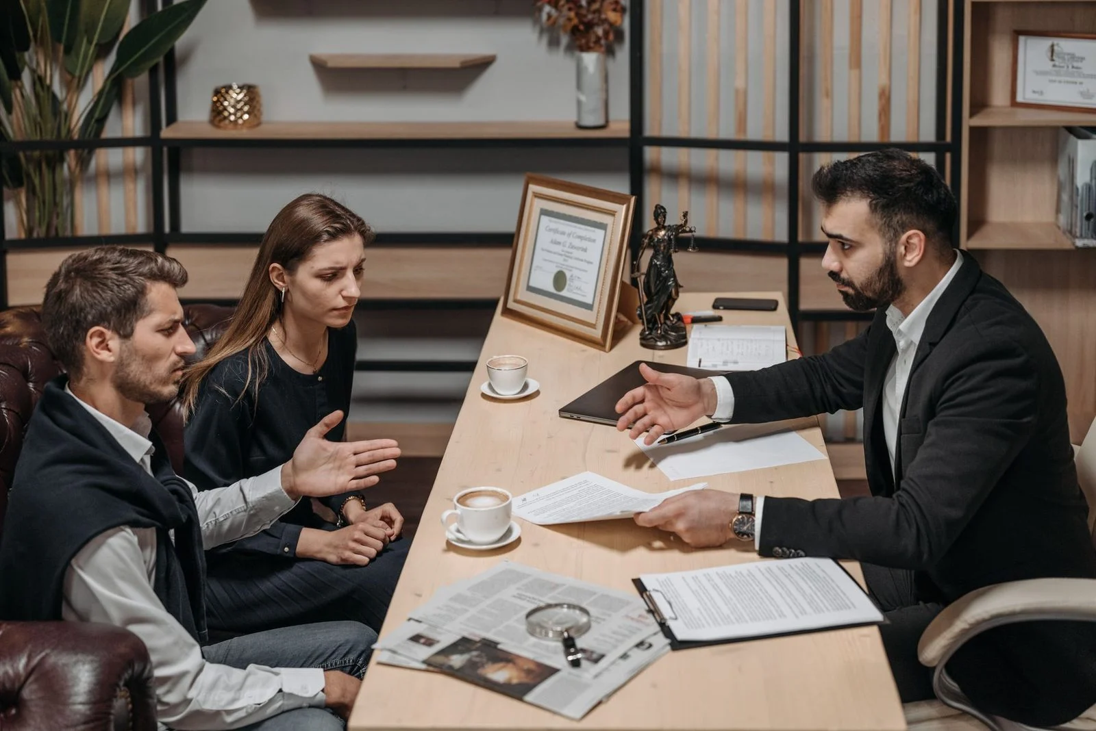 Lawyer meeting with clients at an office table, with documents and coffee in front of them.