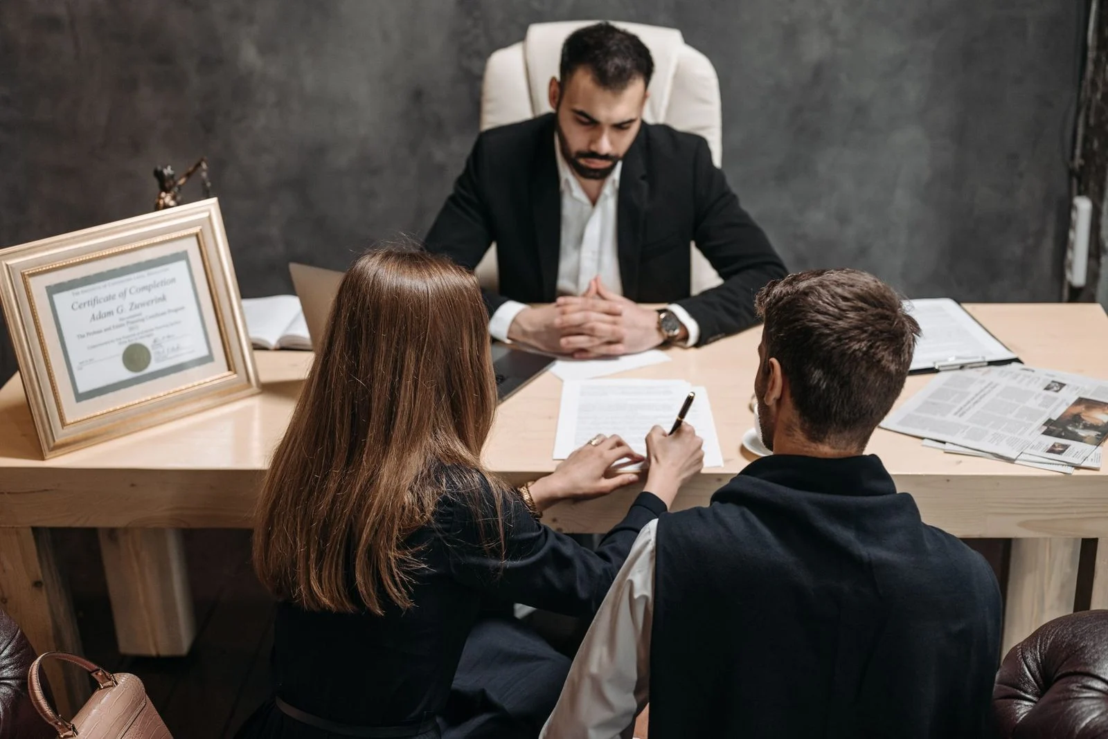 A lawyer reviews legal documents with clients across a desk in an office.