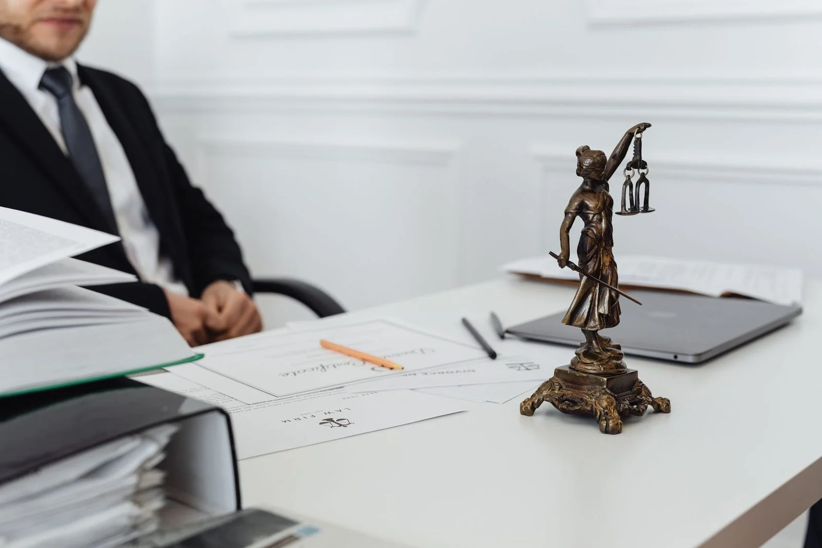 A legal workspace with a Lady Justice statue, stacked documents, and a laptop on a desk.