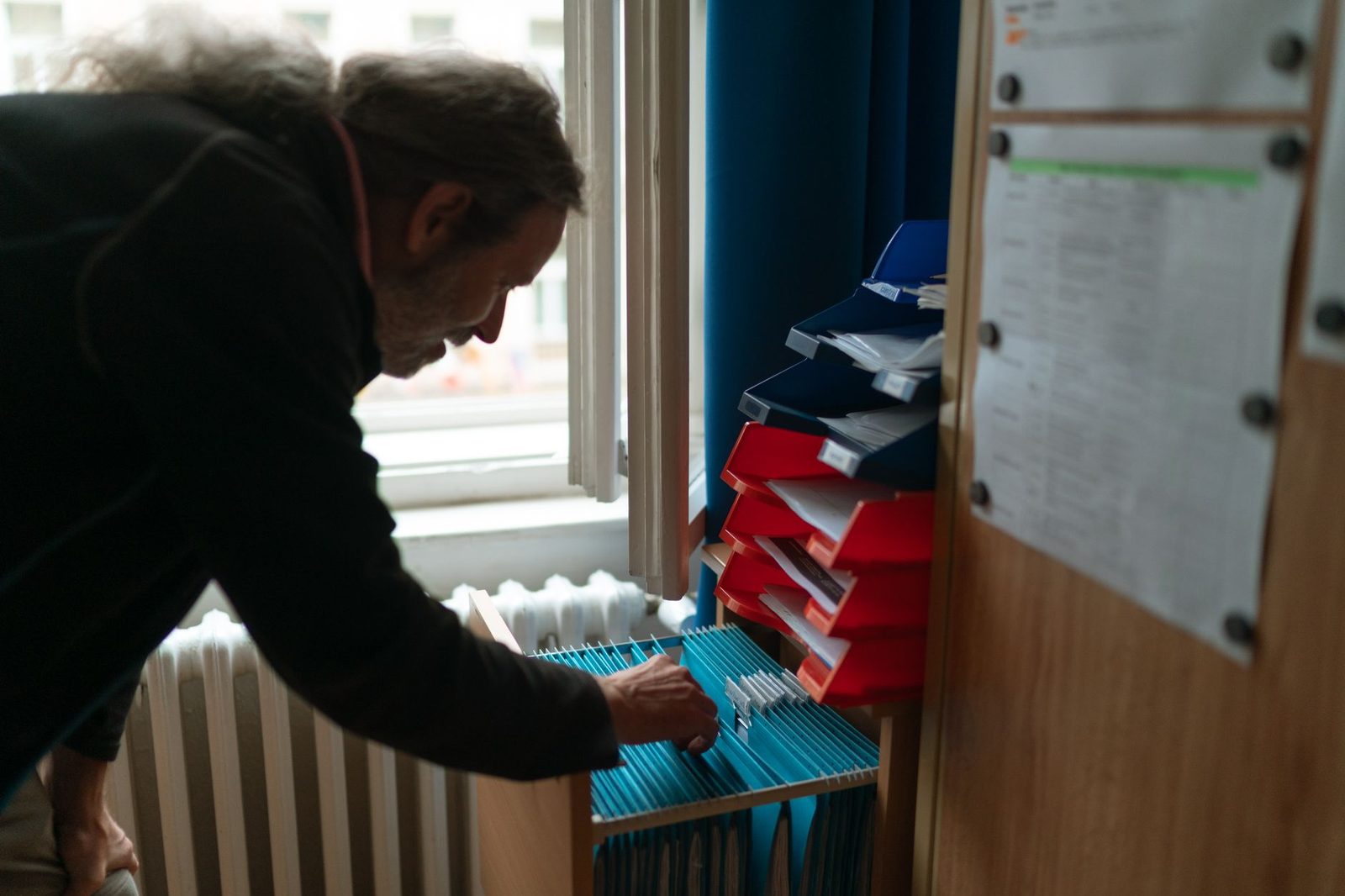 A man with long hair searches through files in an organized office.
