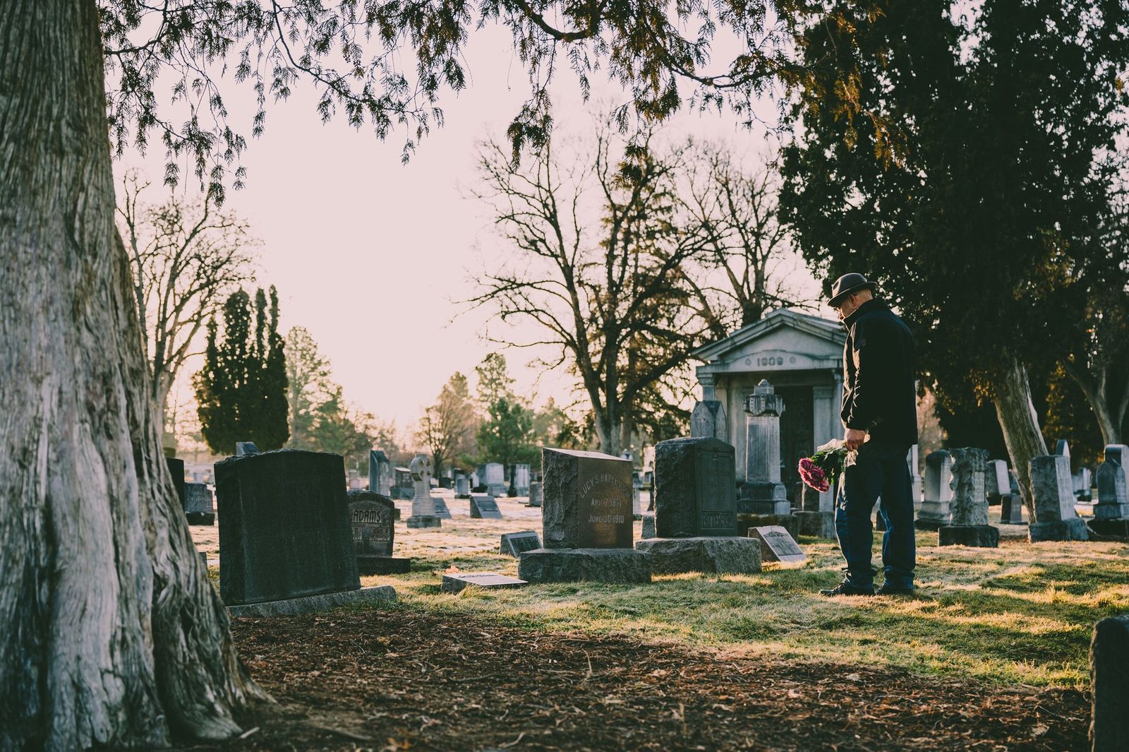 A person holds flowers while standing in a peaceful cemetery.
