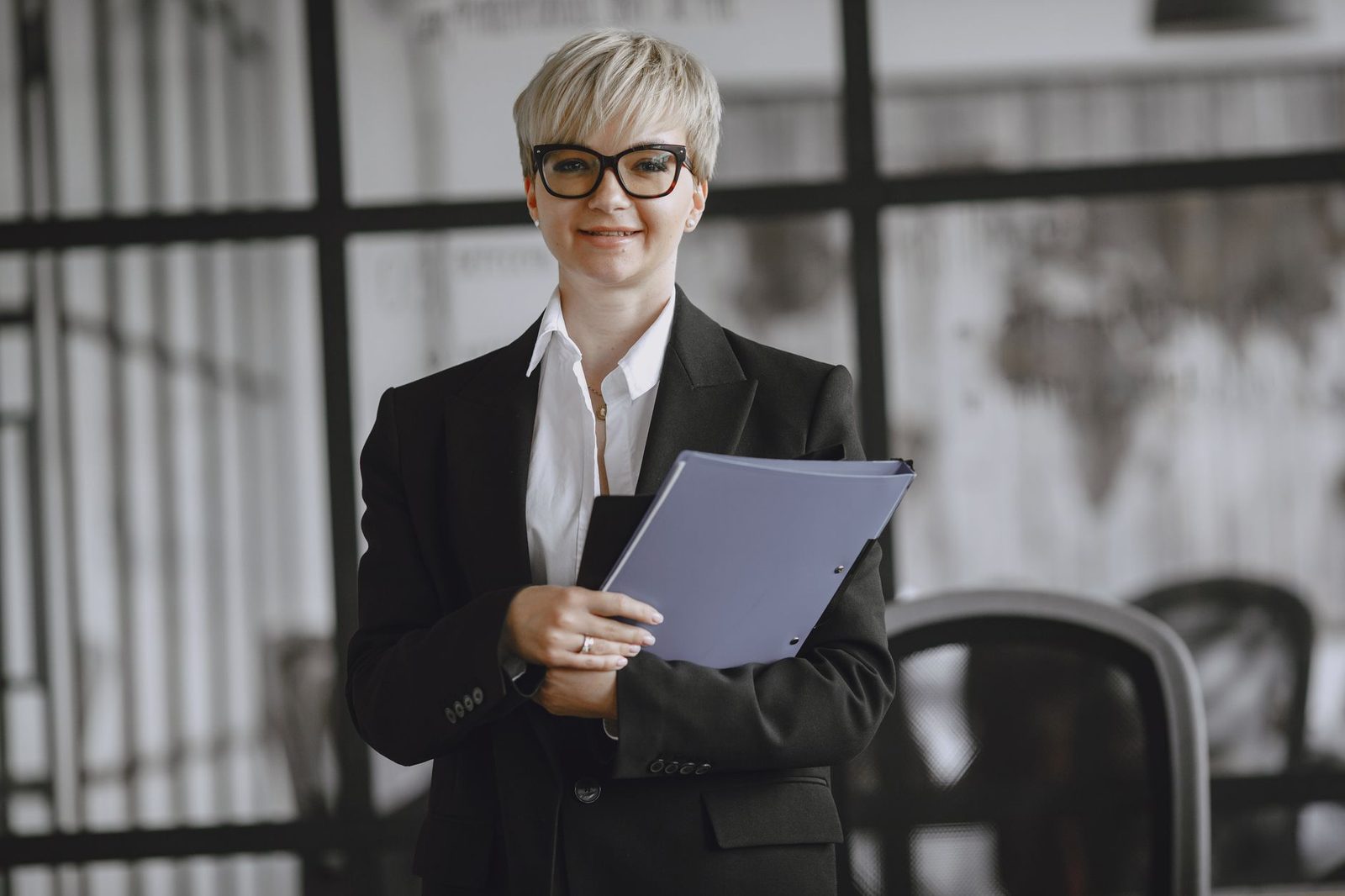 A professional woman in a suit holds a folder in a modern office.