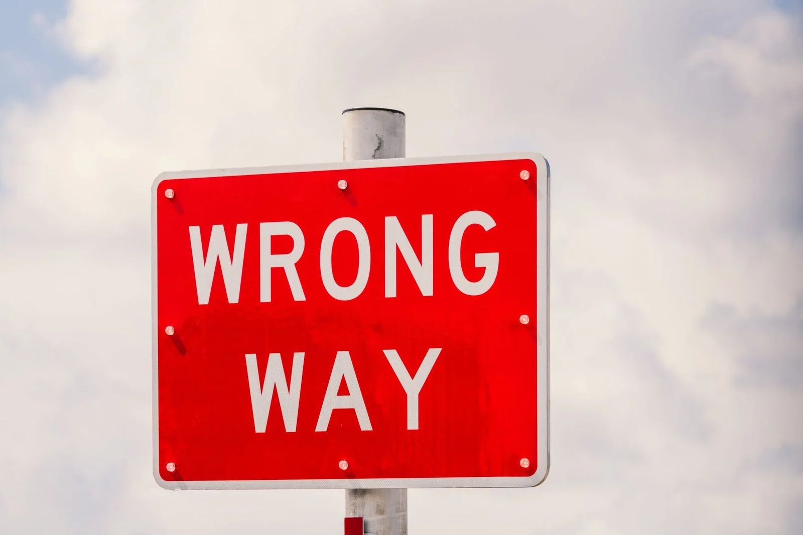 A red "Wrong Way" traffic sign against a cloudy sky in Miami, Florida.
