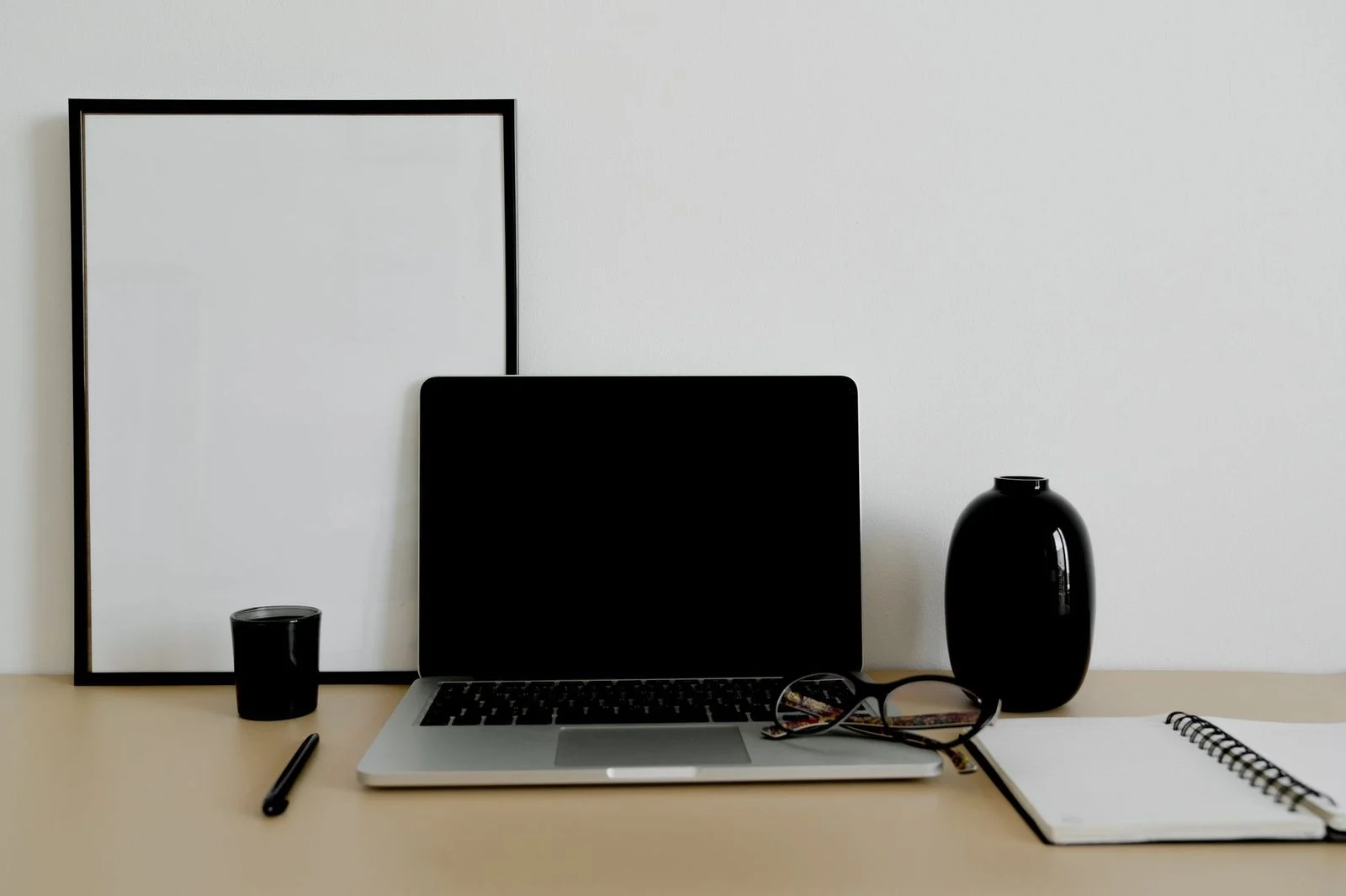 A tidy desk with a laptop, eyeglasses, and stationery arranged in a bright, organized workspace.