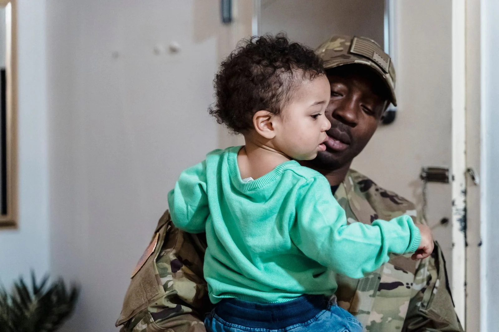 A uniformed military father lovingly holds his young child indoors.