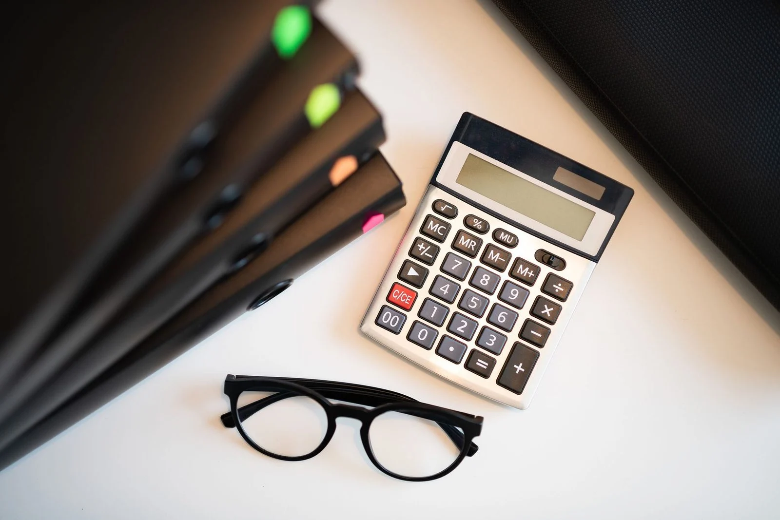 Calculator, eyeglasses, and folders arranged on an office desk.