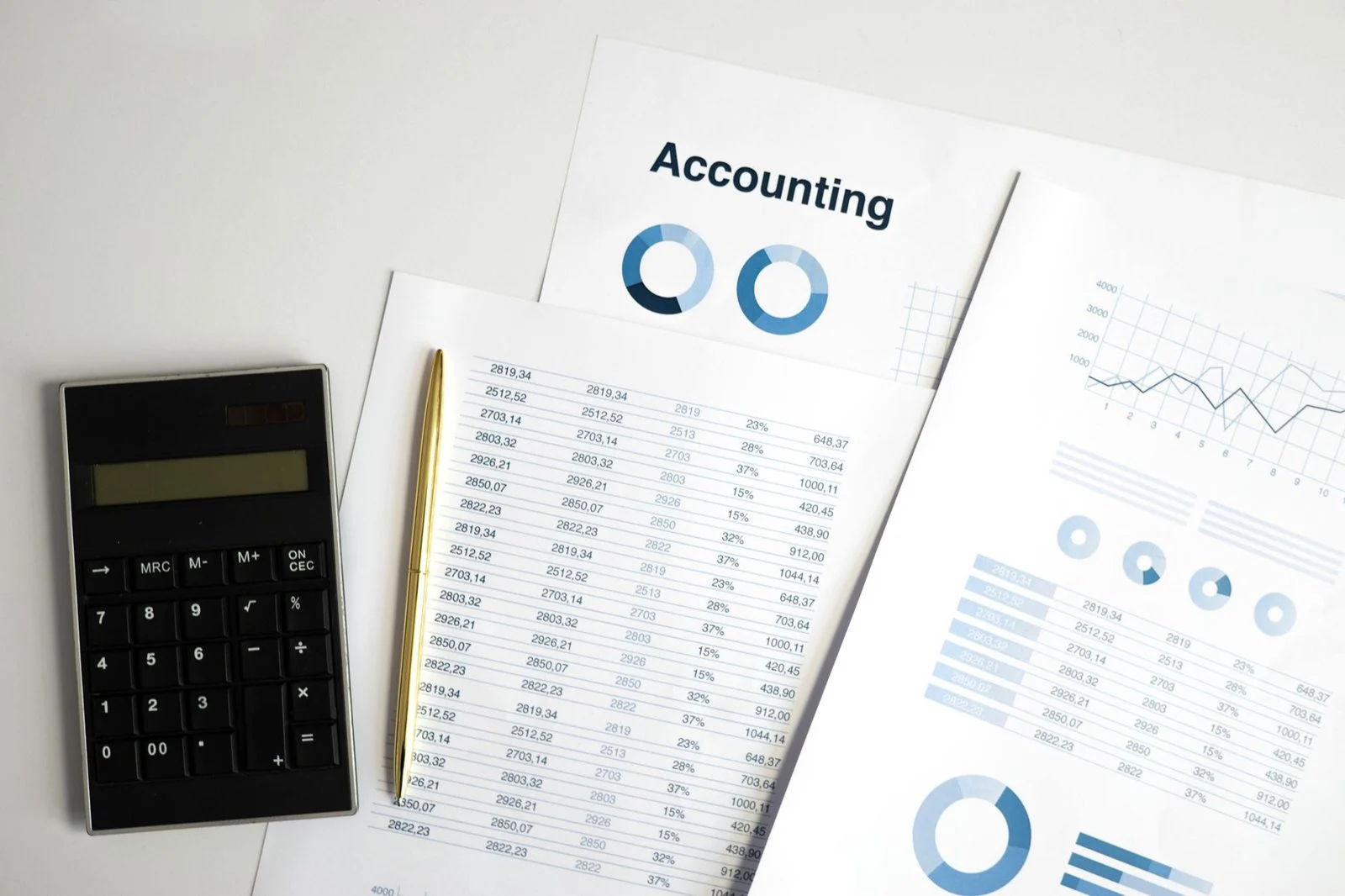 Calculator resting on accounting documents and printed charts across a desk.