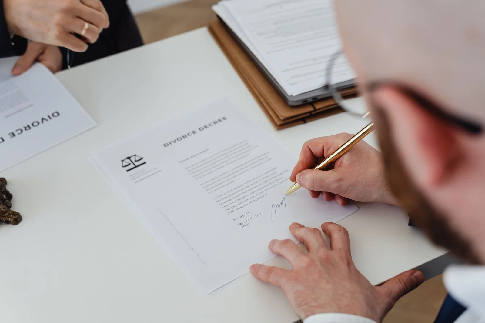 Primer plano de una mano firmando un documento de divorcio sobre un escritorio de madera.