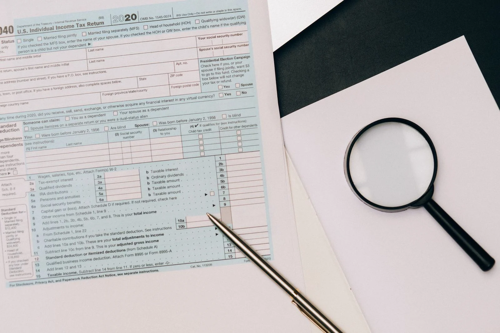 A close view of a tax return form with a pen and magnifying glass resting on it.