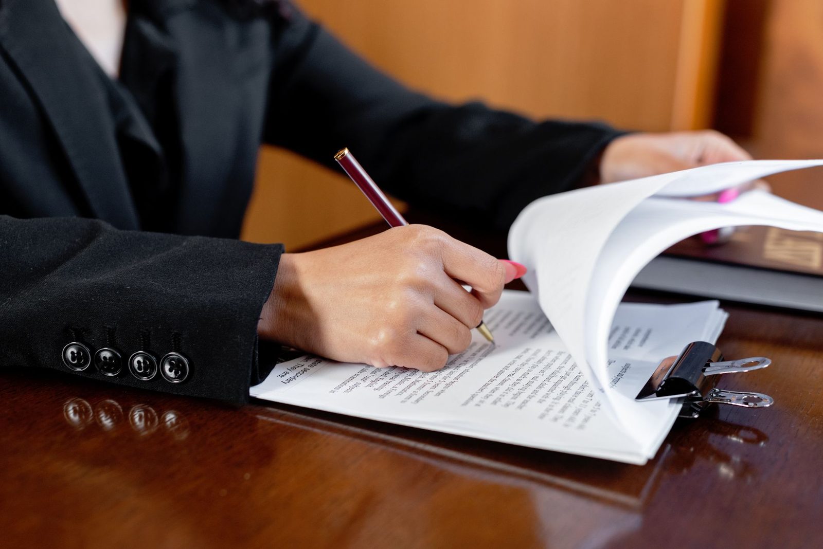 Close-up of a woman signing legal documents with a pen in a bright office setting.