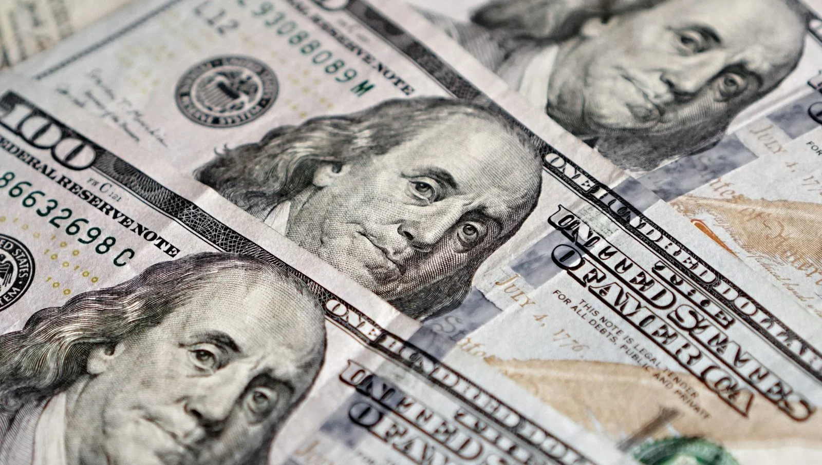 Close-up of several US $100 bills, each showing Benjamin Franklin's portrait.