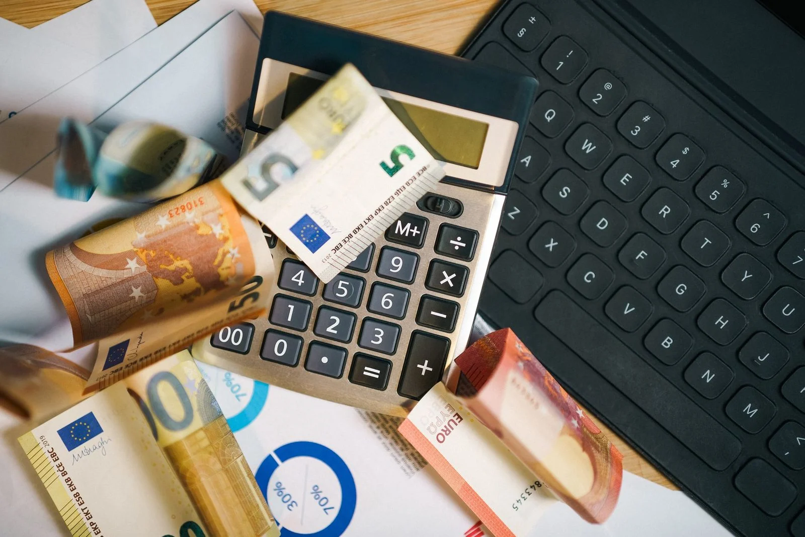 Euro banknotes, a calculator, and a laptop keyboard arranged on a desk for financial analysis.