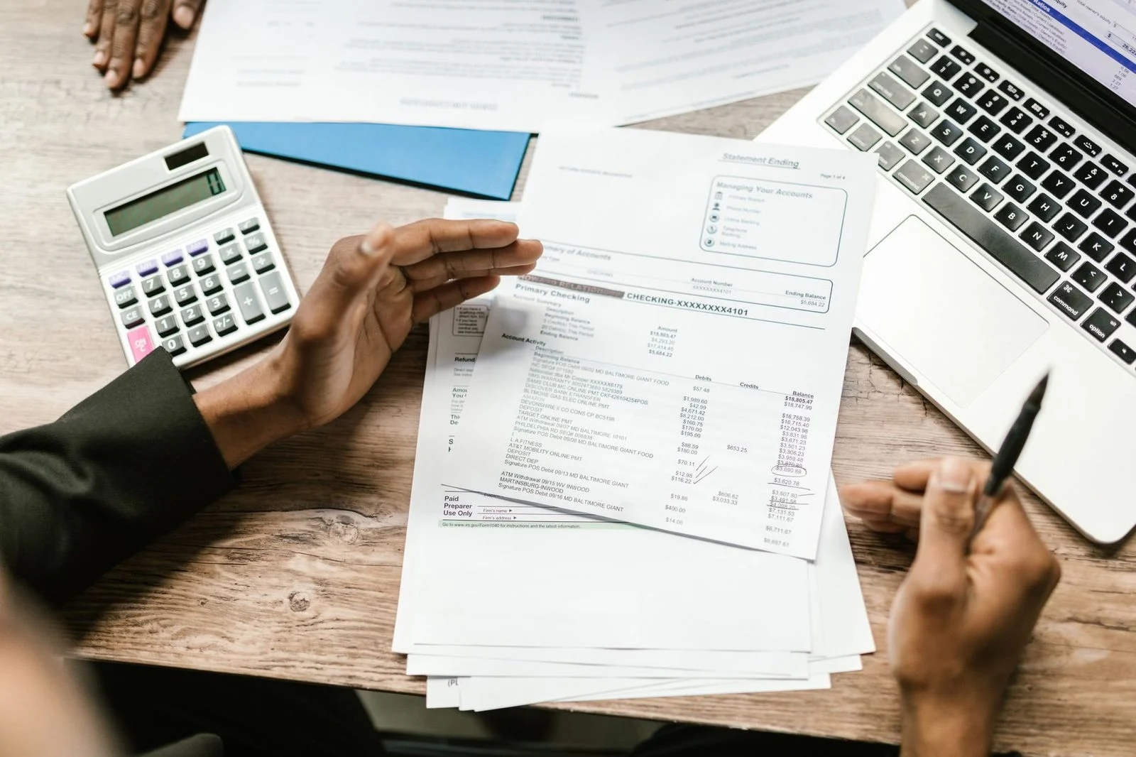 Hands hold financial documents beside a calculator and laptop on an office desk.