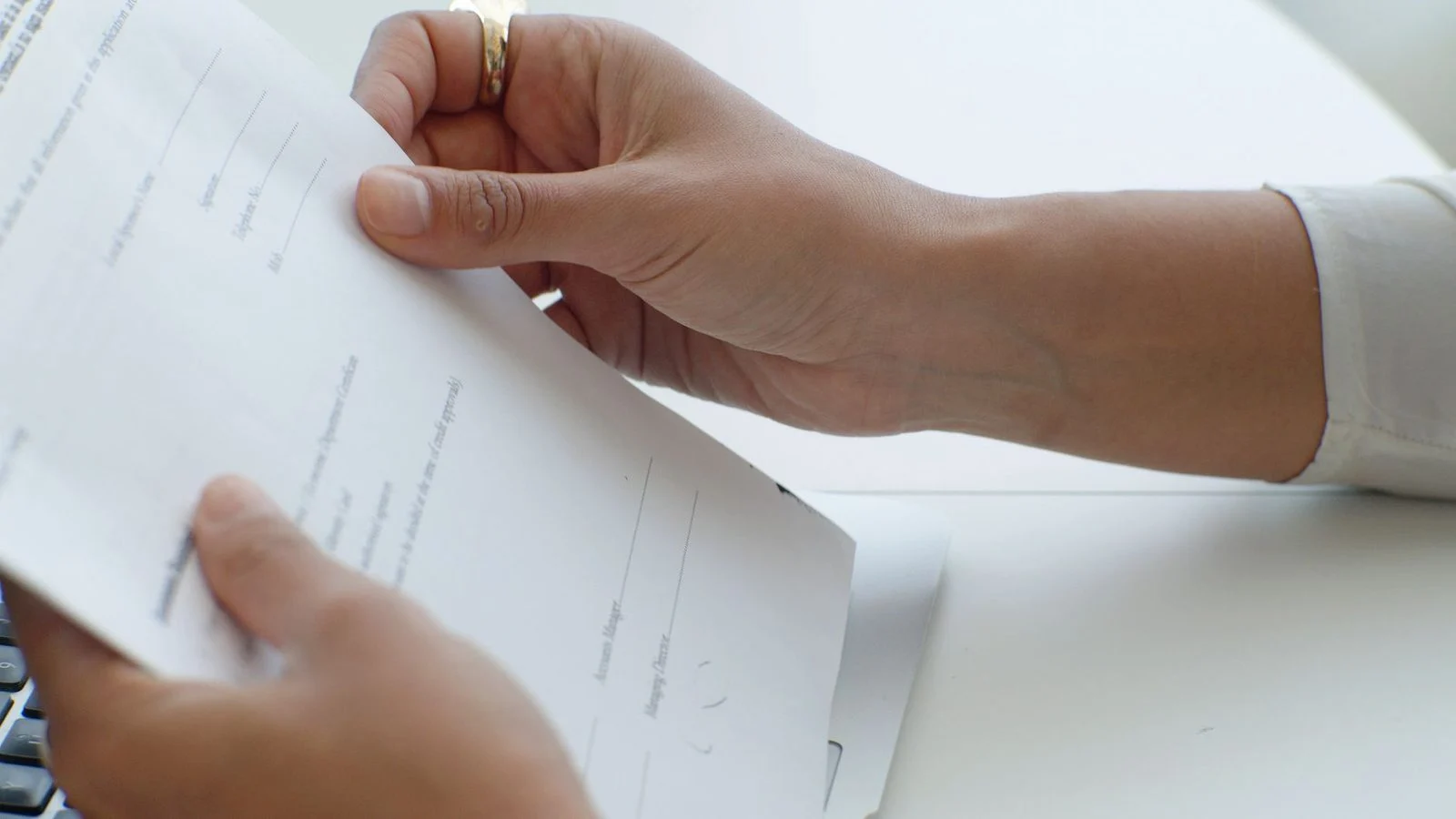 Hands holding a document above a keyboard on an office desk.