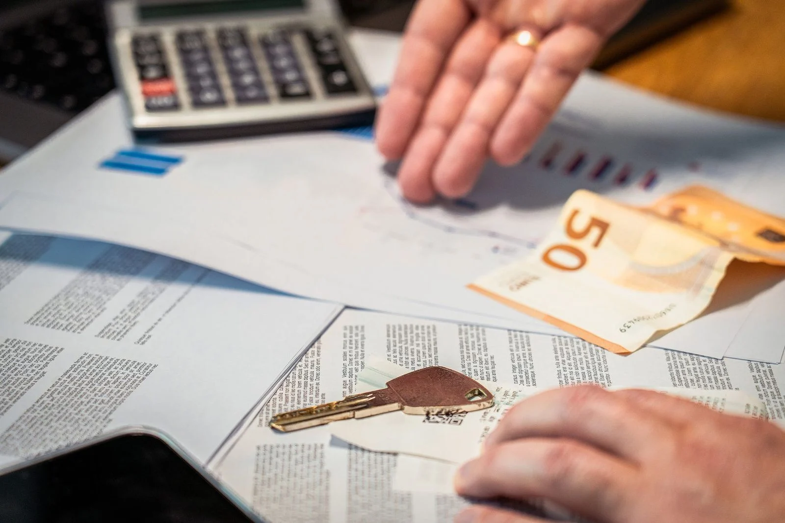 Hands sorting financial papers beside a 50 euro banknote and a key.