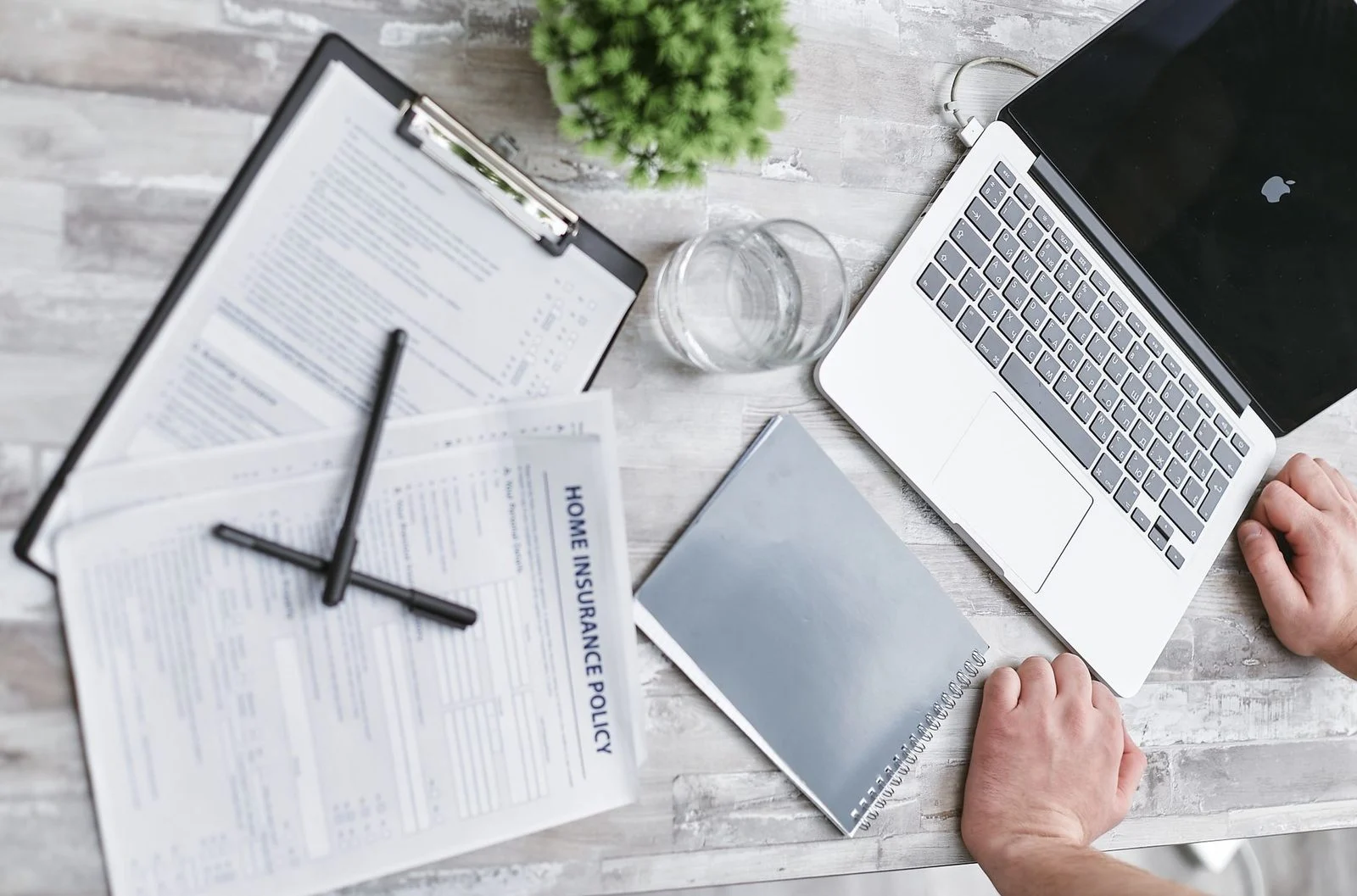 Home insurance forms, a laptop, and documents spread across a desk in a professional office setting.