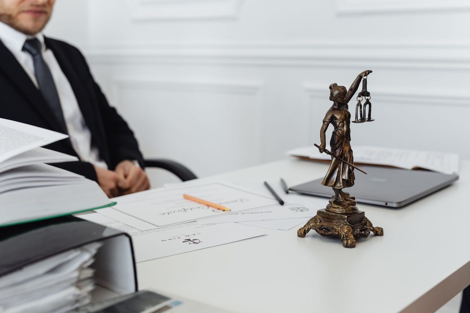 Lady Justice statue beside legal documents and a laptop on a law office desk.