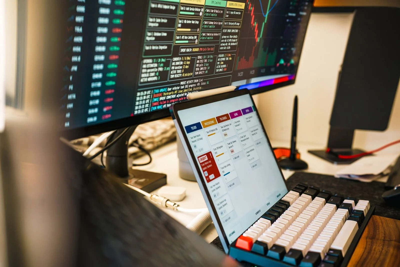 Modern workspace with trading monitors and a tablet displaying project management tools.