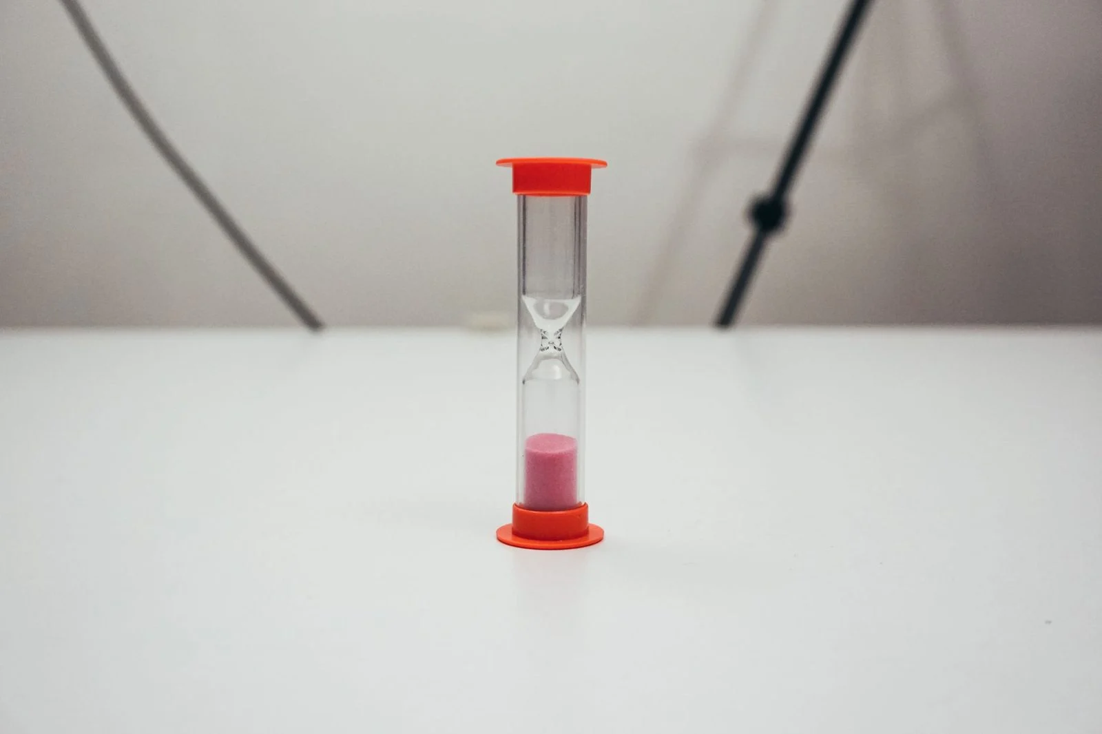 Red-topped hourglass filled with pink sand against a plain background.
