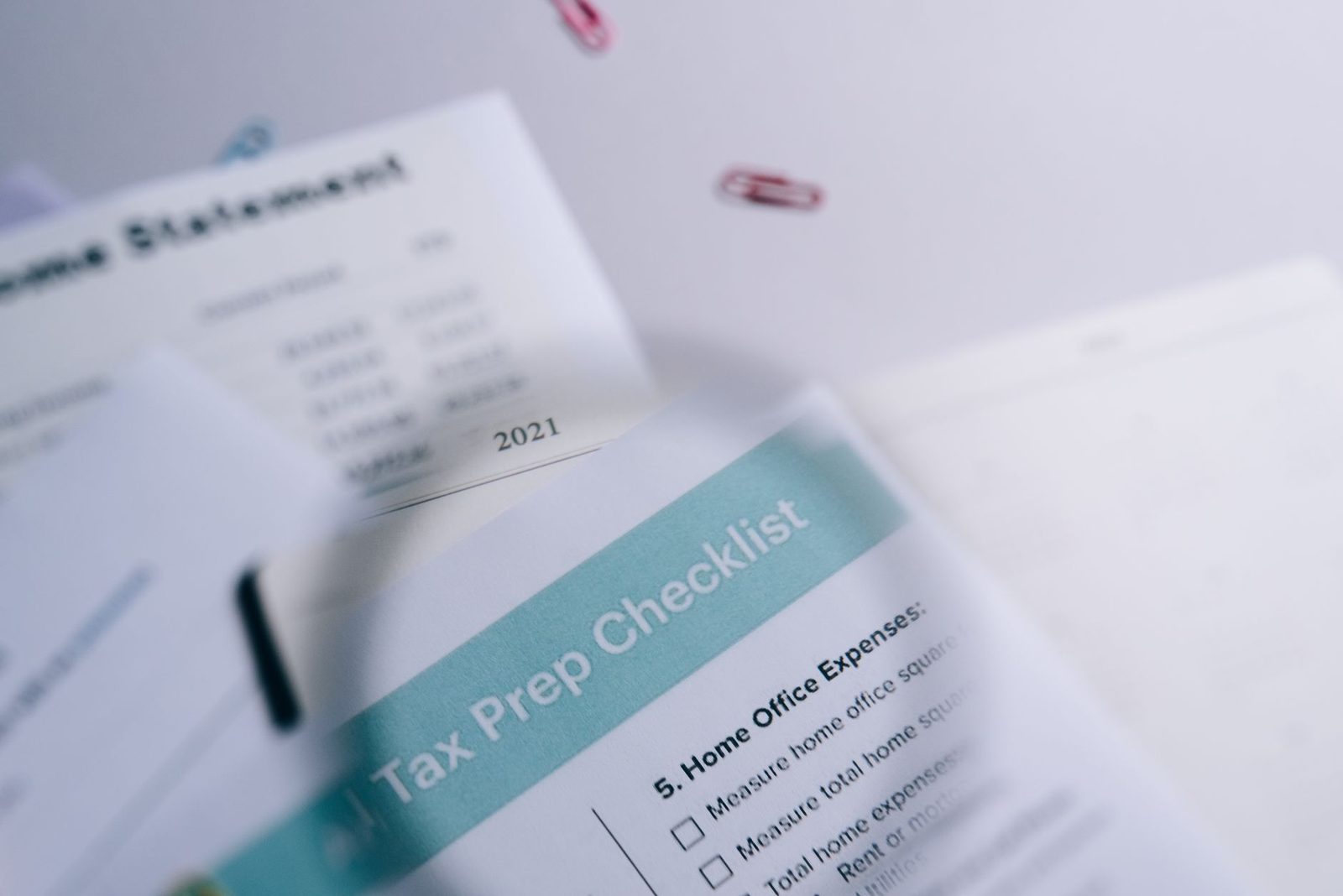 Tax preparation checklist and income statement with paperclips on desk.