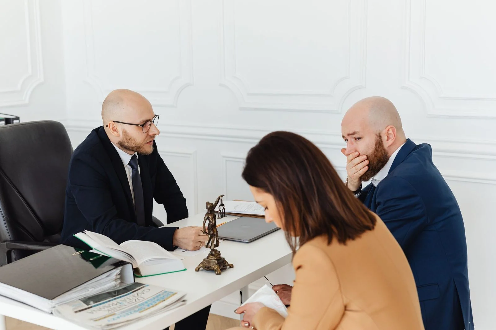 Three adults sit across a desk from one another in a professional office during a serious legal consultation.