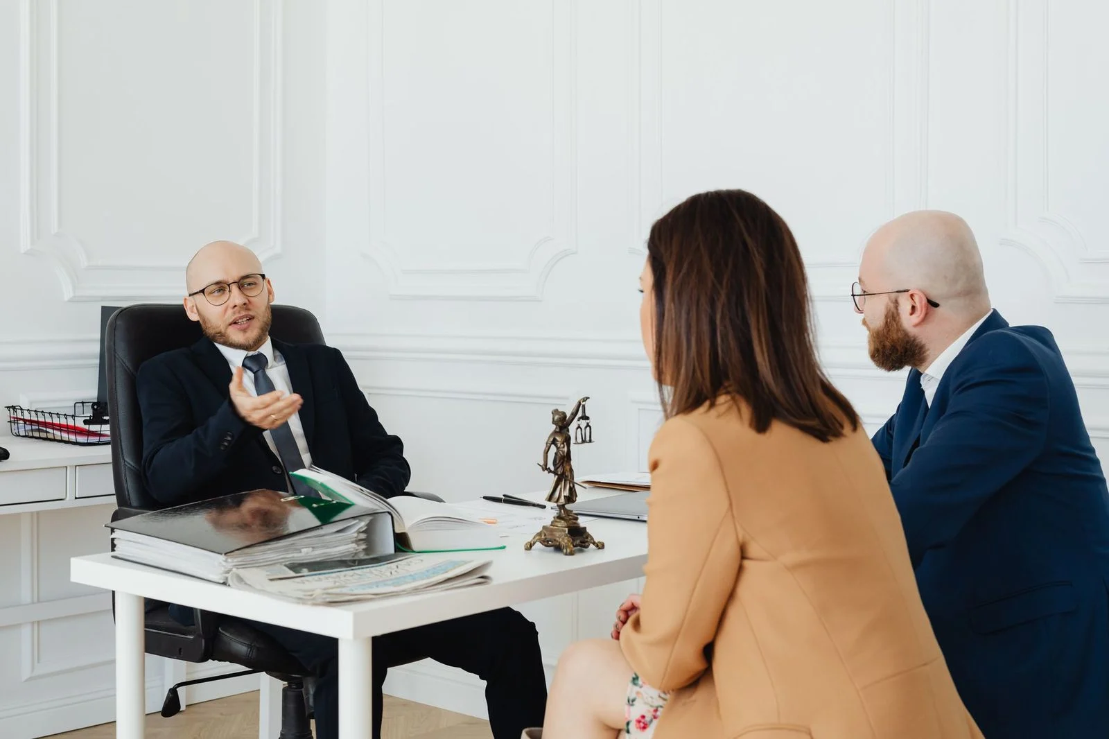 Three adults sit at a conference table in an office, reviewing documents during a legal discussion.