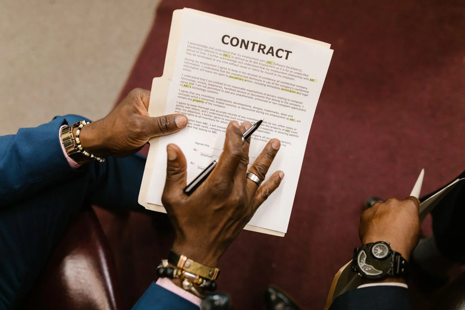 Two businessmen review and sign a contract together at a desk in an office.