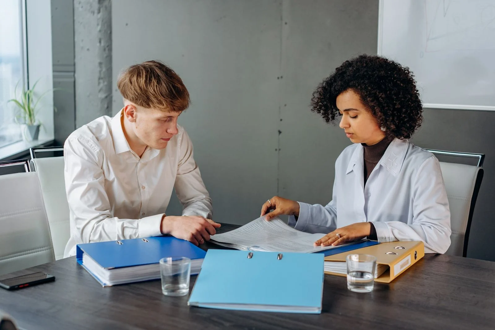 Two colleagues review business documents together at an office desk.