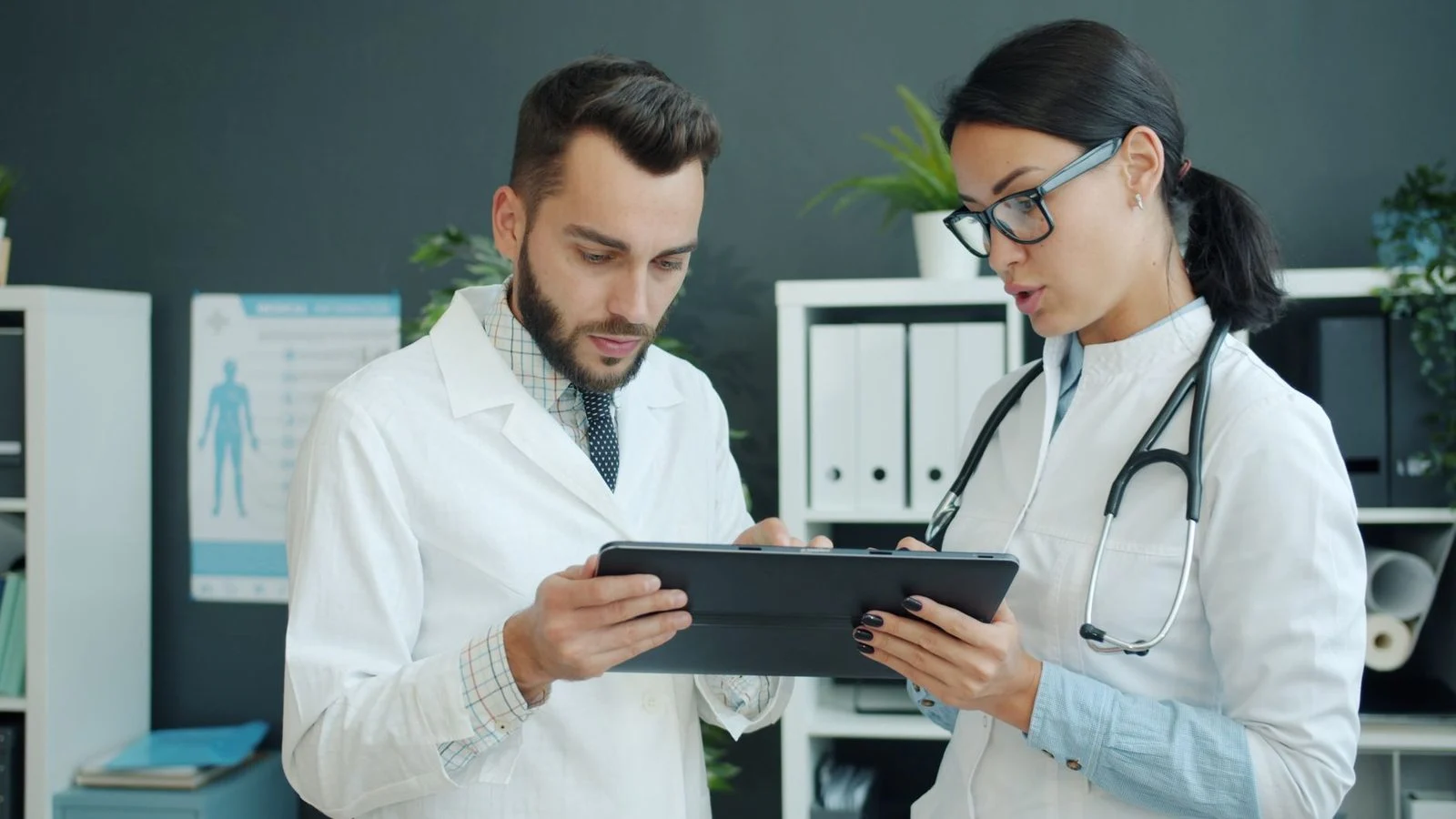 Two doctors review medical information together on a tablet in a clinical setting.