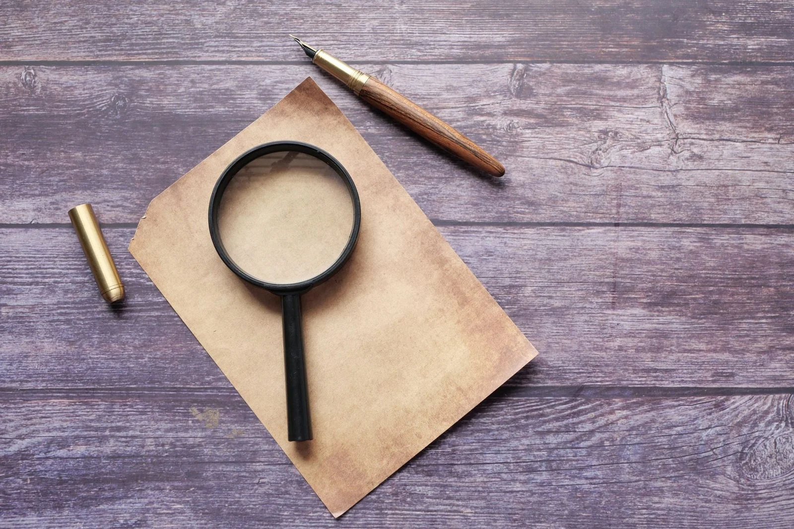 Vintage quill pen and magnifying glass resting on a rustic wooden surface.
