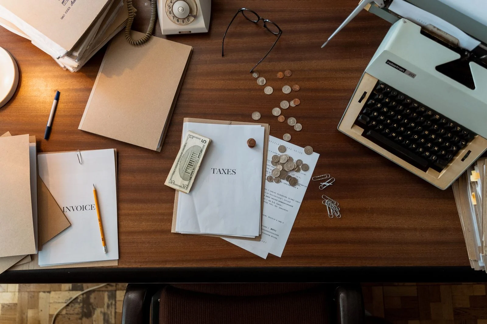 Vintage typewriter, scattered coins, and paperwork on a wooden desk.
