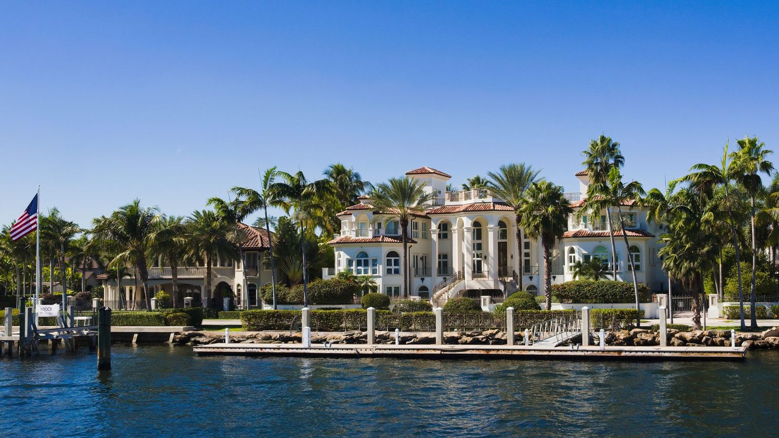 Waterfront mansion with palm trees under a clear blue sky.