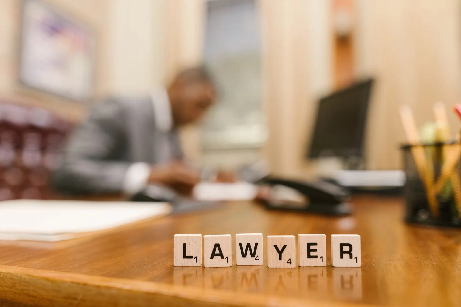 Wooden letter tiles spelling "LAWYER" sit on a desk in a blurred office.