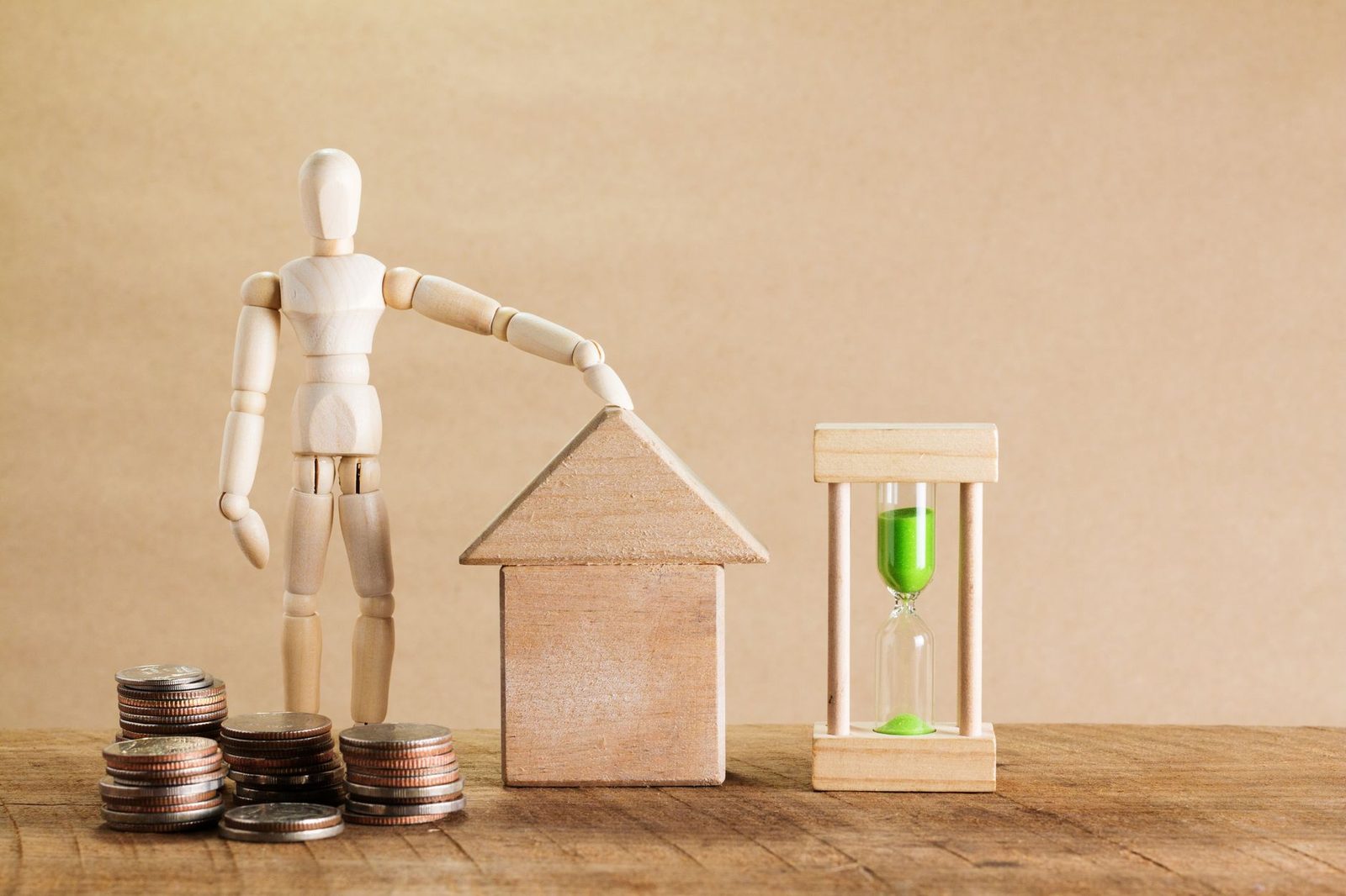 Wooden mannequin beside a model house, coins, and an hourglass, representing estate and financial planning.