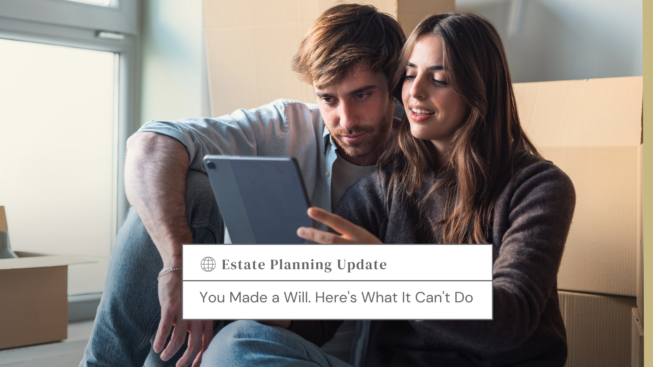 Couple sits among moving boxes, looking at a tablet together in a bright room.